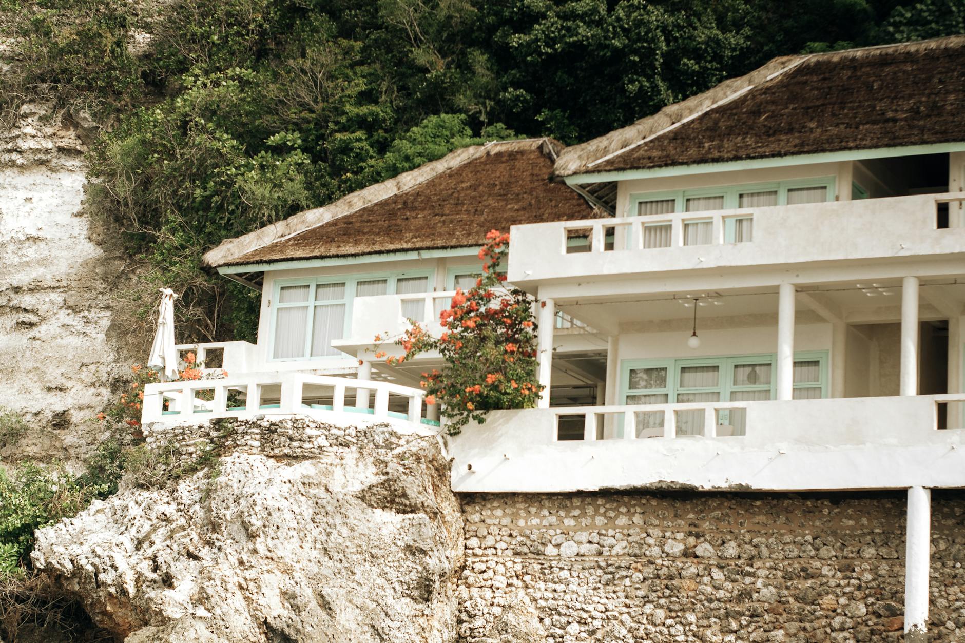 Beautiful villa perched on a cliff overlooking the ocean, surrounded by lush greenery.